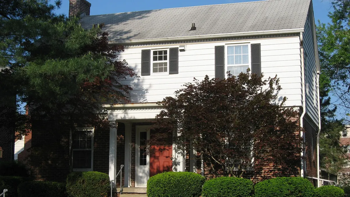 A white two-storey house with dark shutters and a red front door